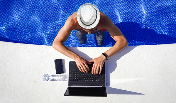 Barbat in piscina, lucrand la laptop, cu telefon mobil alaturi